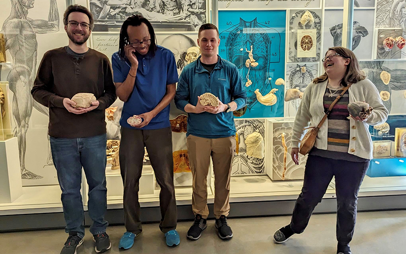 Three men and a woman laugh and smile as they hold petrified examples of human organs.